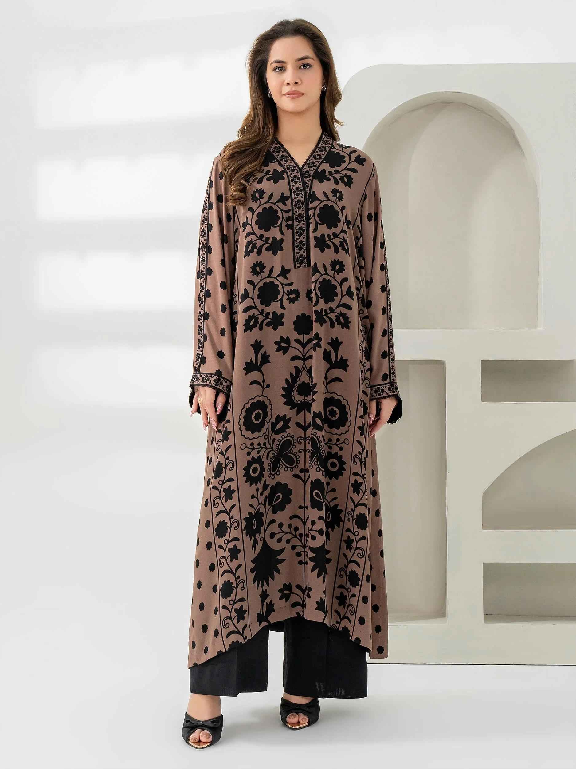 A woman wearing a long, loose-fitting brown and black printed kurta paired with black trousers stands against a minimal white background.