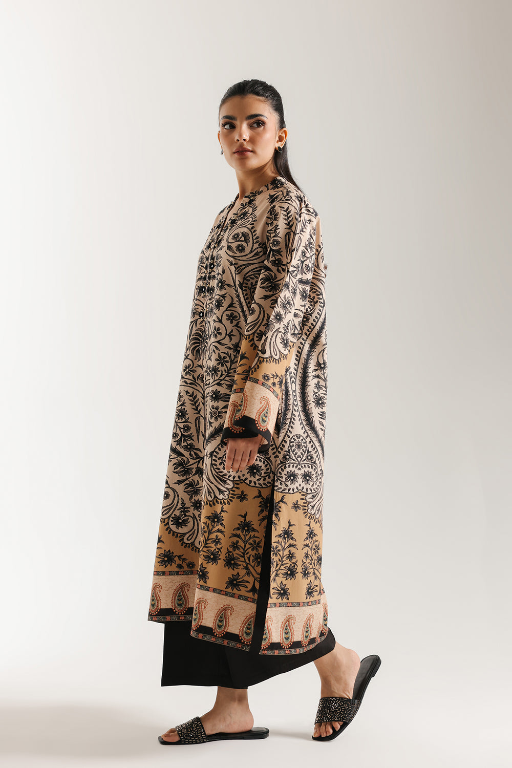 Woman sitting on a chair wearing ethnic pakistani a patterned outfit against a white background