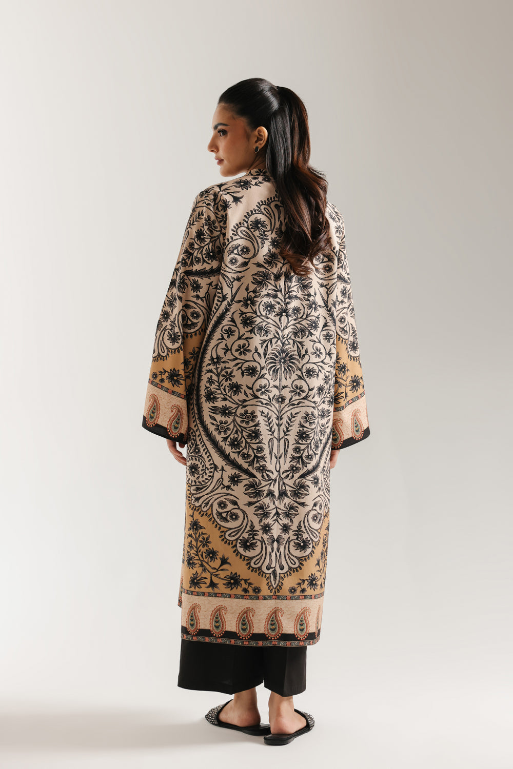 Woman sitting on a chair wearing ethnic pakistani a patterned outfit against a white background