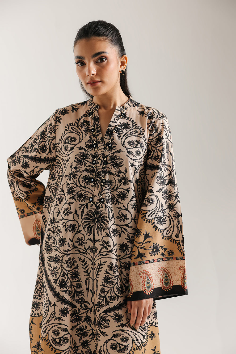 Woman sitting on a chair wearing ethnic pakistani a patterned outfit against a white background