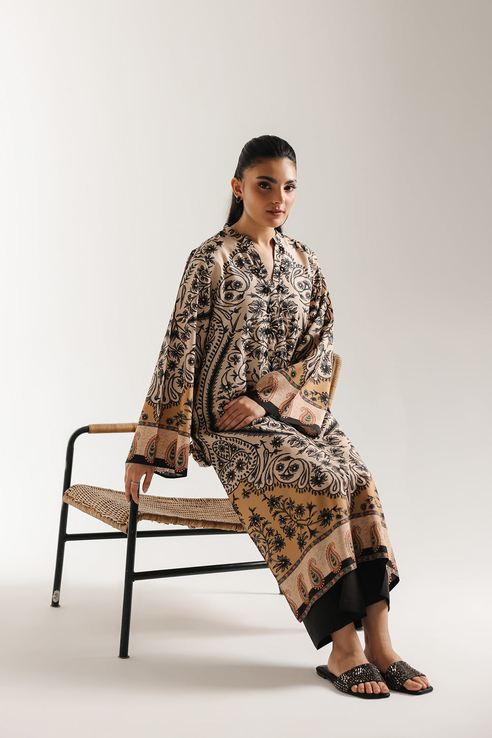 Woman sitting on a chair wearing ethnic pakistani a patterned outfit against a white background