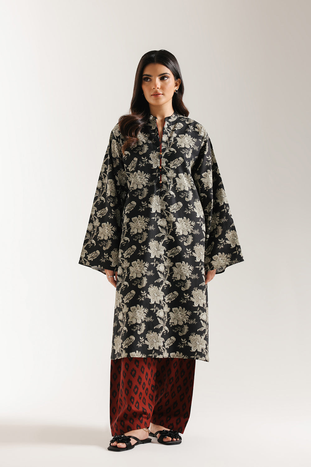 Woman wearing ethnic black floral long shirt with red shalwar on a white background