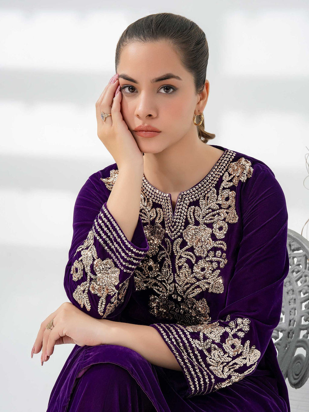 Woman wearing a purple outfit with intricate gold embroidery against a neutral background