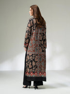 Woman wearing a long printed silk shirt in black and earthy tones with floral patterns and button detailing, paired with black trousers
