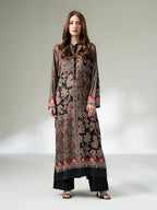 Woman wearing a long printed silk shirt in black and earthy tones with floral patterns and button detailing, paired with black trousers