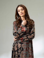 Woman wearing a long printed silk shirt in black and earthy tones with floral patterns and button detailing, paired with black trousers
