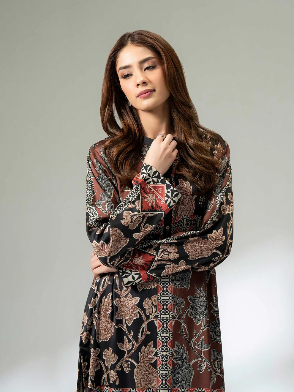 Woman wearing a long printed silk shirt in black and earthy tones with floral patterns and button detailing, paired with black trousers