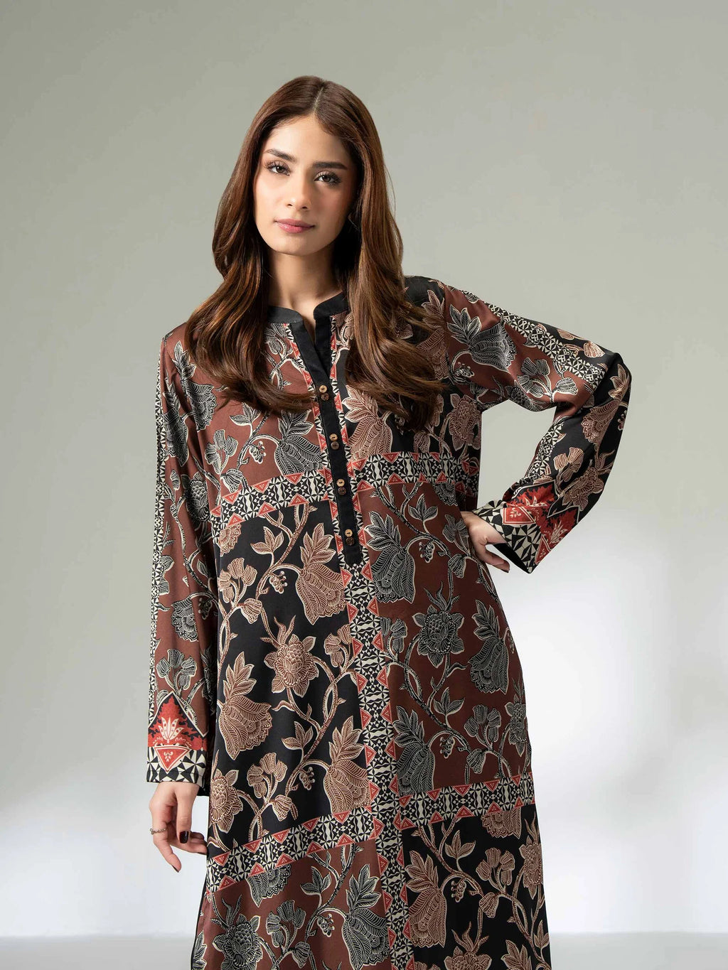 Woman wearing a long printed silk shirt in black and earthy tones with floral patterns and button detailing, paired with black trousers