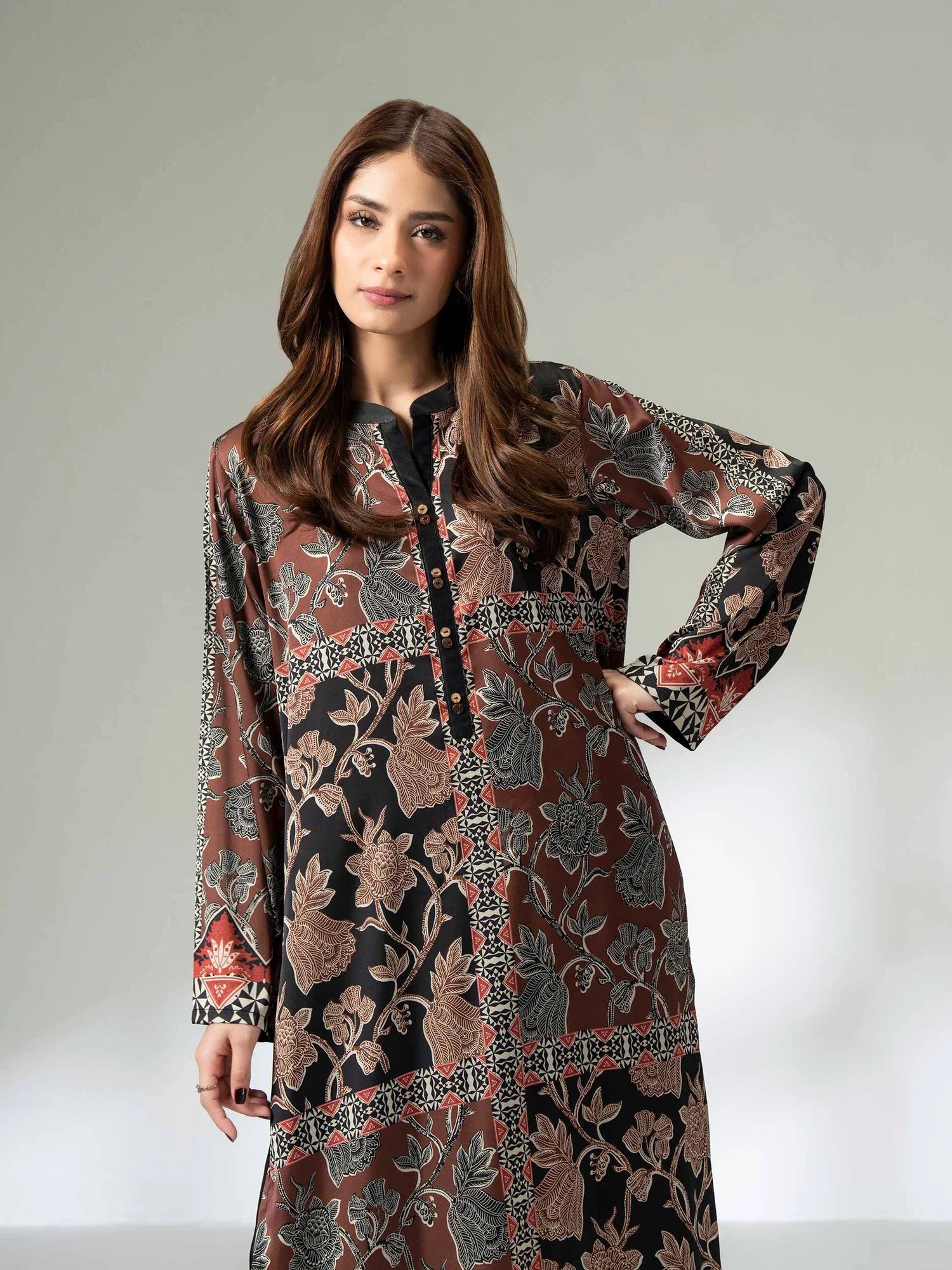 Woman wearing a long printed silk shirt in black and earthy tones with floral patterns and button detailing, paired with black trousers