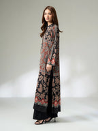 Woman wearing a long printed silk shirt in black and earthy tones with floral patterns and button detailing, paired with black trousers