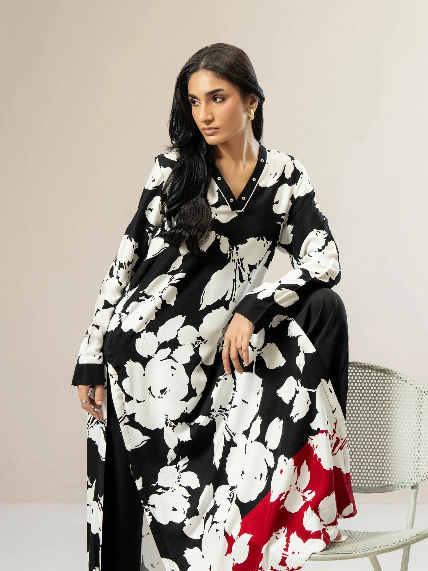 Woman wearing a black and white floral dress with a red bottom section, sitting on a chair.