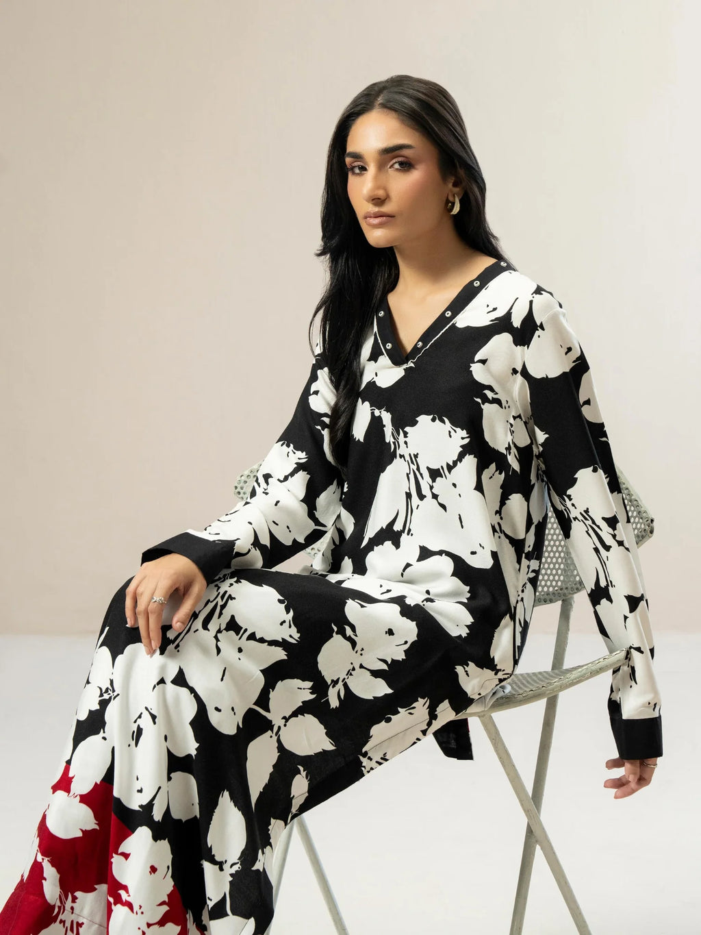 Woman wearing a black and white floral dress sitting on a chair against a plain background