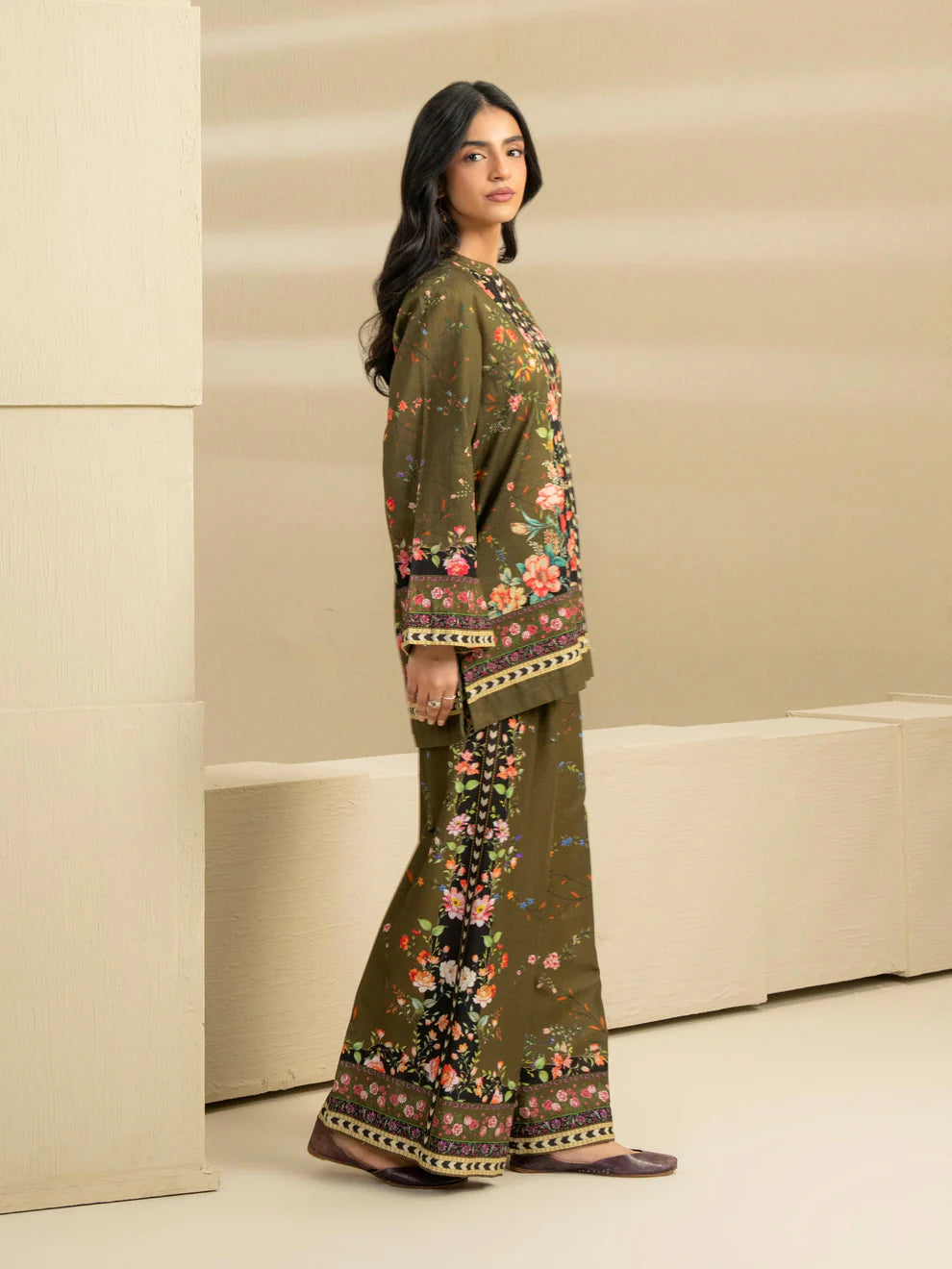 Woman wearing a floral embroidered outfit against a beige wall.