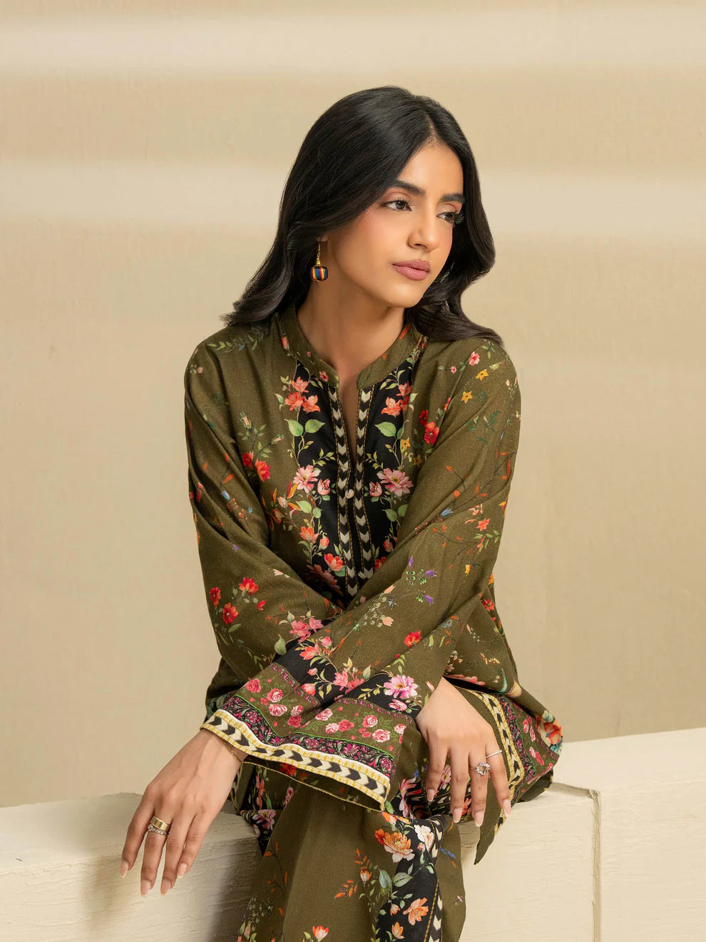 Woman wearing a green embroidered traditional outfit against a beige background