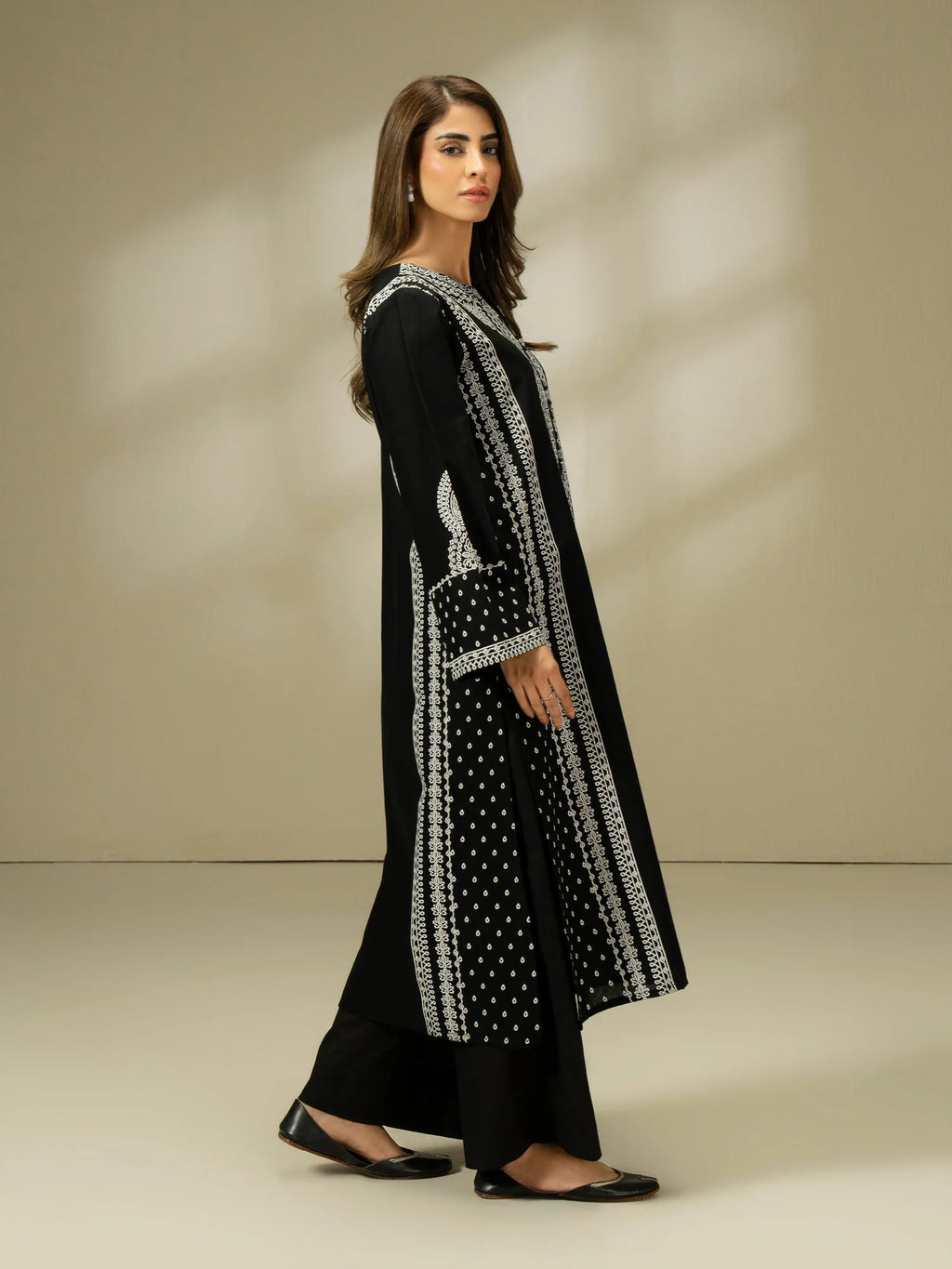 Woman wearing a black and white embroidered outfit on a beige background
