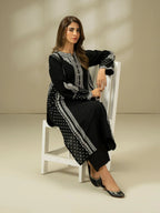 Woman sitting on a white chair wearing a black and white patterned outfit against a beige background