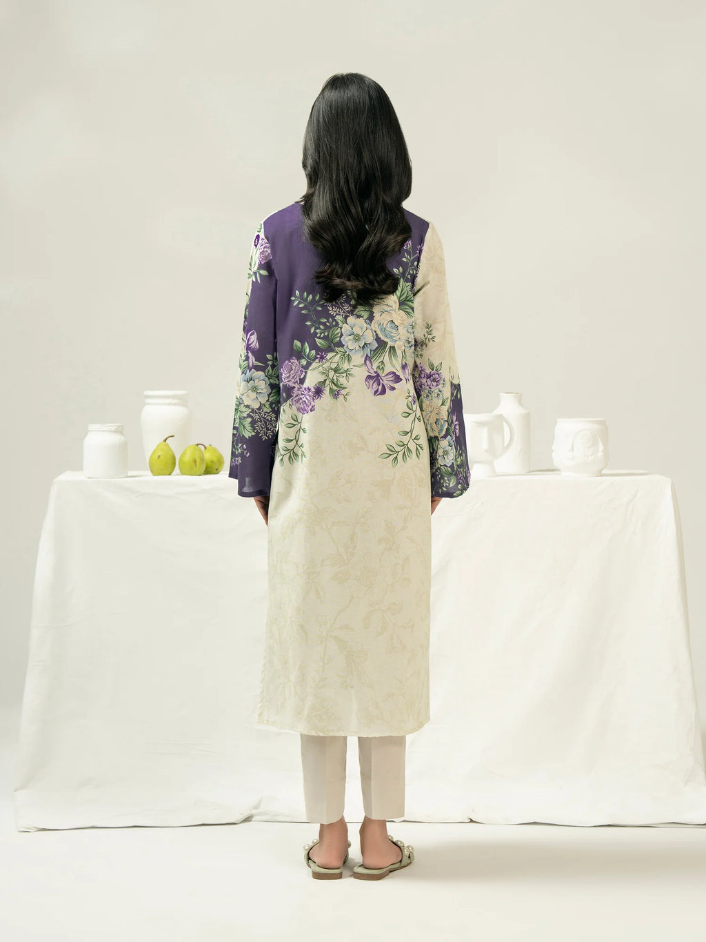 Person wearing a floral dress with a purple top and white apron in a minimalistic setting.