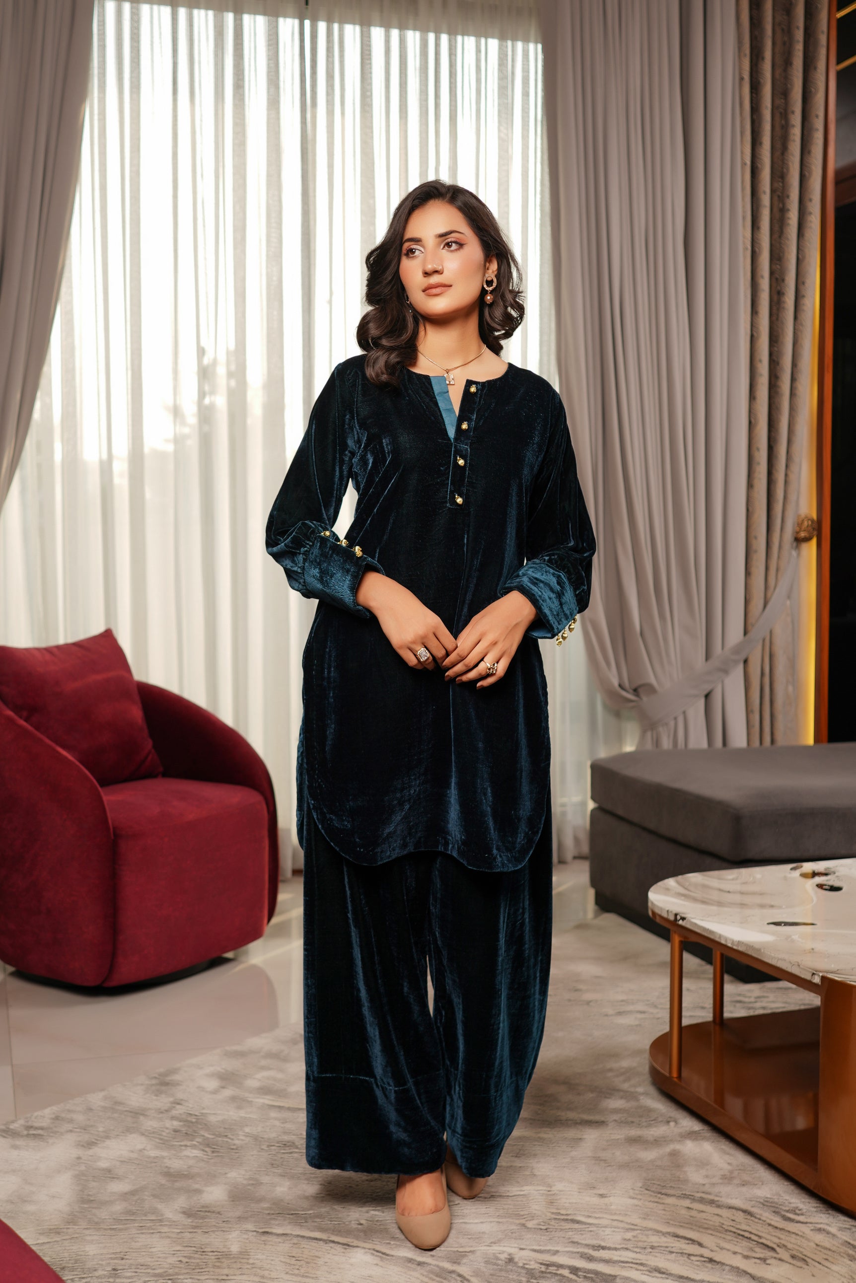 Woman in a dark blue velvet outfit standing in a modern living room.