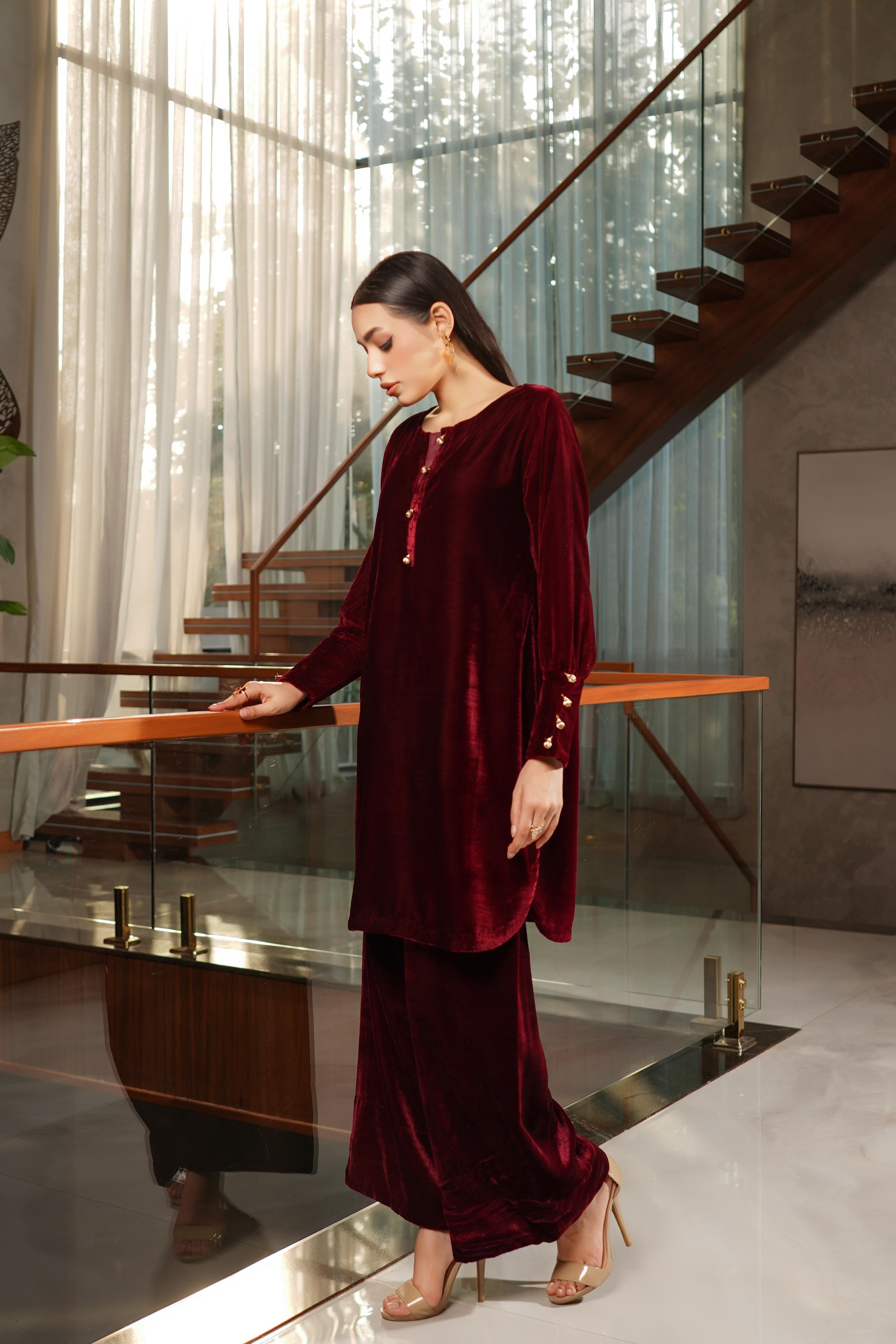 Woman in a burgundy velvet outfit standing in a modern interior setting.