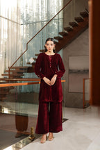 Woman in a burgundy outfit standing in a modern interior setting with stairs and glass walls.