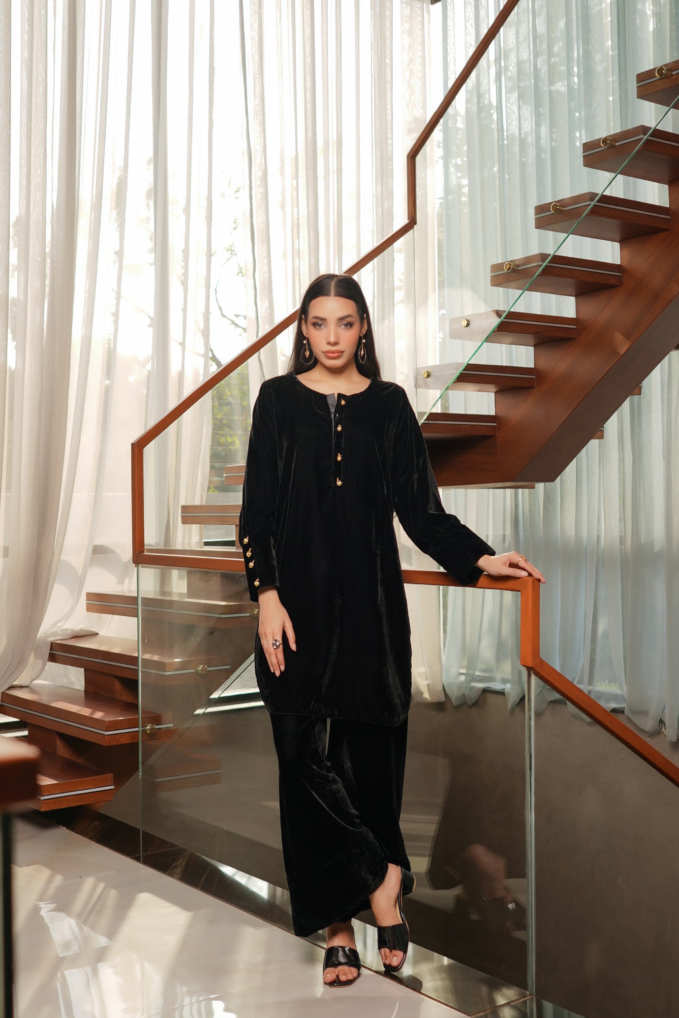 Woman in a black outfit standing on a modern staircase with glass railings.