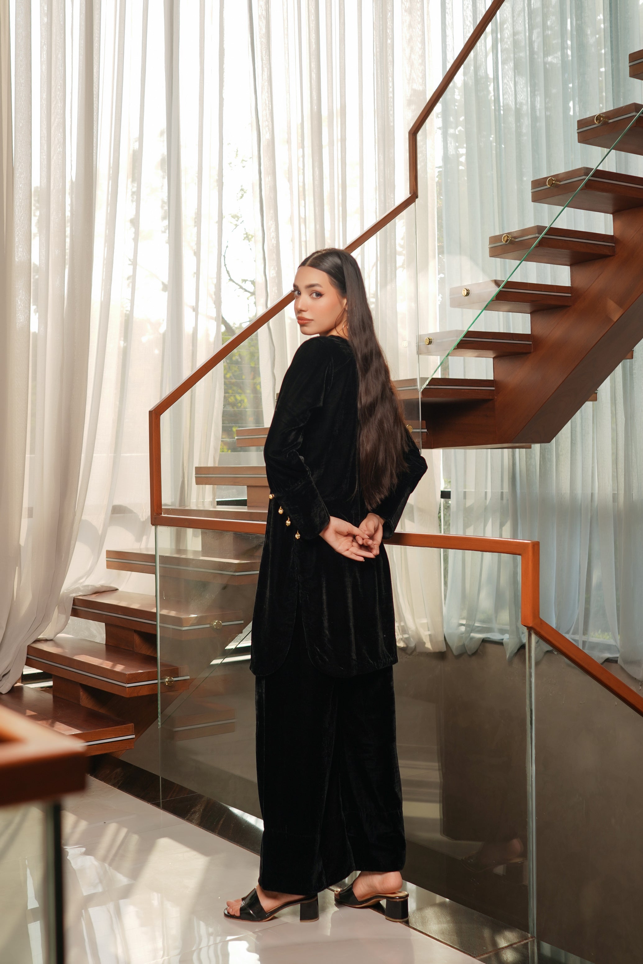 Woman in a black outfit standing on a modern staircase with glass railings.