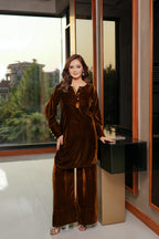 Woman in a brown velvet outfit standing in a modern room with large windows.
