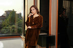 Woman in a brown velvet outfit standing in a room with large windows.