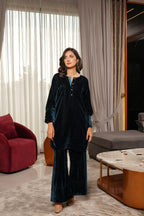 Woman in a dark blue velvet outfit standing in a modern living room.