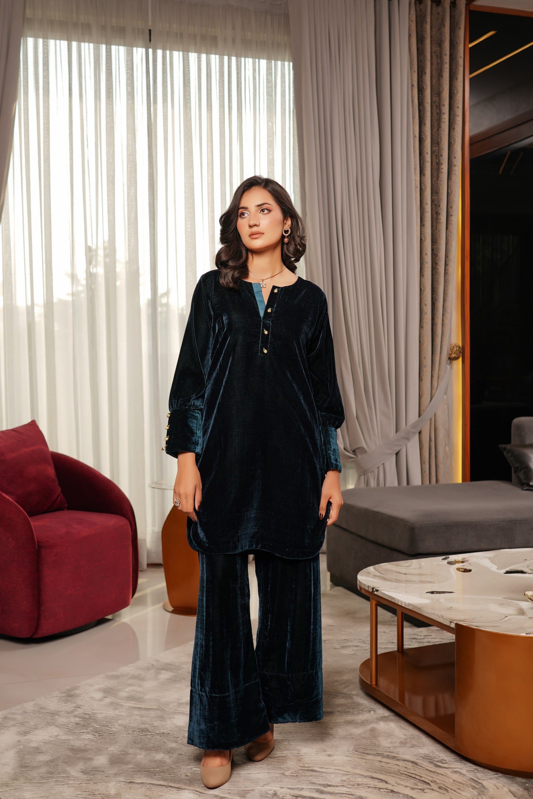 Woman in a dark blue velvet outfit standing in a modern living room.